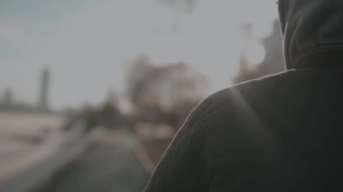 Sokakta yürüyen kapüşonlu bir adamın arka görüntüsü. Video kaydı. Gençler kaldırımda gün batımına doğru ilerliyorlar..