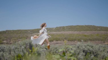 Genç bir kadın beyaz elbiseyle sahada çok güzel koşuyor. Başla. Beyaz elbiseli bir kadının tarlada yavaşça koştuğu hafiflik ve özgürlük hissi. Kadınlar beyaz elbiseler ve saçlar yavaşça gelişir.