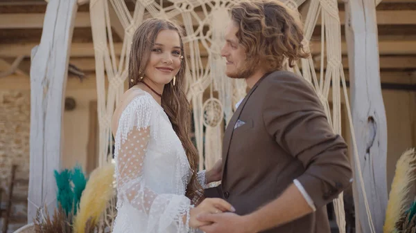 Hochzeit im Hippie-Stil. Handeln. Schönes Brautpaar tauscht Ringe unter Krone aus. Hippie-Frischvermählte verloben sich in schönen Outfits vor dem Hintergrund der geflochtenen Krone — Stockfoto