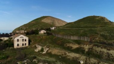 Tepelerin arasındaki terk edilmiş köyün havadan görüntüsü. Vuruldu. Resimli dağlar ve uçurumlar mavi gökyüzü arka planında ender bulunan eski evleri olan yeşil çayırlarla kaplıdır..