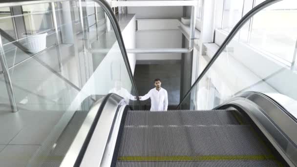 Beyaz tişörtlü bir adam iş merkezinin içinde yürüyen merdivenden çıkıyor. HDR. Mağazadaki yürüyen merdivendeki genç adam.. — Stok video