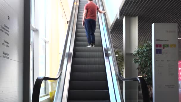 Ένας άντρας με κόκκινο μπλουζάκι ανεβαίνει τις κυλιόμενες σκάλες μέσα στο επιχειρηματικό κέντρο. HDR. Νεαρός στις κυλιόμενες σκάλες στο πολυκατάστημα. — Αρχείο Βίντεο