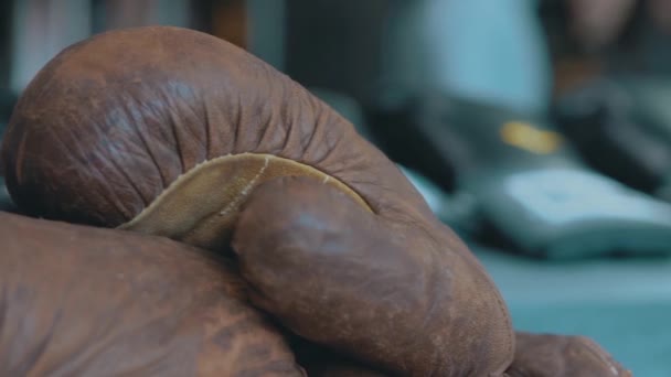 Zbliżenie starych brązowych skórzanych rękawic bokserskich na rozmytym tle. Nagranie. Pojęcie sprzętu sportowego i sportowego. — Wideo stockowe