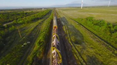Yeşil alan arka planındaki yük treninin üst görüntüsü. Vuruldu. Drone treni hızla takip ediyor. Güneşli bir günde yeşil tarlanın arka planında demiryolu yüklü tren yolculukları