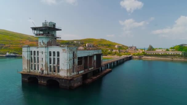 Fábrica abandonada con muelle en la costa. Le dispararon. Hermoso muelle con edificio de fábrica abandonado o empresa de pesca. La fábrica secreta abandonada para la producción de los torpedos en la Crimea — Vídeo de stock