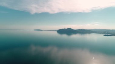 Dağ kıyısında aynalı deniz yüzeyi. Vuruldu. Su, şafak vakti, dağ kıyısının arka planında mavi gökyüzünü yansıtır. Aynalı suyla resimli deniz manzarası