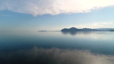 Mavi gökyüzünün ayna suyundaki güzel yansıması. Vuruldu. Dağların arka planında denizdeki gökyüzünün yansıması olan resmedilmiş deniz manzarası. Sabah mavi gökyüzü su yüzeyine yansıyor.
