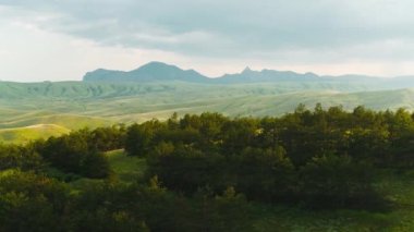 Güneşli bulutlu havada güzel yeşil dağlar ve tepelerin manzarası. Vuruldu. Bulutlu gökyüzü ve güneşin arka planında yeşil tepeler olan dağ manzarası. Bitkilerle dolu yaz yeşil dağları