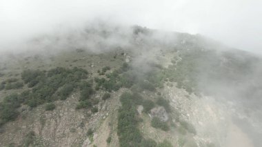 Sisli yamaçtaki dağın zirvesine güzel bir uçuş. Vuruldu. İnsansız hava aracı yoğun sis ile yeşil dağa çıktı. Sisli kefen içinde güzel dağ yamaçlarının manzarası.