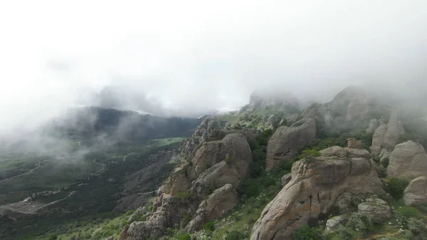 Extrém repülés sziklás hegyeken ködben. Lelőtték. Lélegzetelállító kilátás sziklás lejtőin zöld hegyek a ködben. Top kilátás ködös hegyek sziklás szegélyek — Stock Fotó