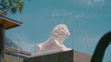 Mavi arka planda güzel bir aslan heykeli. Başla. Beyaz doğalcılık abidesi. Aslan heykeli. Gökyüzünün arka planında yaslanmış beyaz aslan heykeli