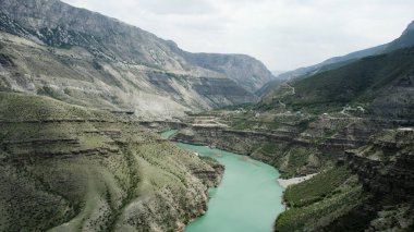 Kayaların arasında akan kıvrımlı yeşil bir nehrin havadan görünüşü. Başla. Resimli bir deresi ve dağ sırası olan yaz doğal manzarası.