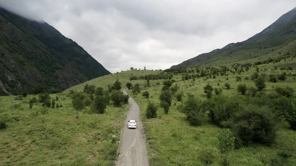 Vue aérienne d'une voiture blanche se déplaçant sur la route rurale de montagne le long de la nature sauvage. L'action. Voiture conduisant sur la route droite pendant le voyage d'été et les vacances le long des arbres rares. — Photo