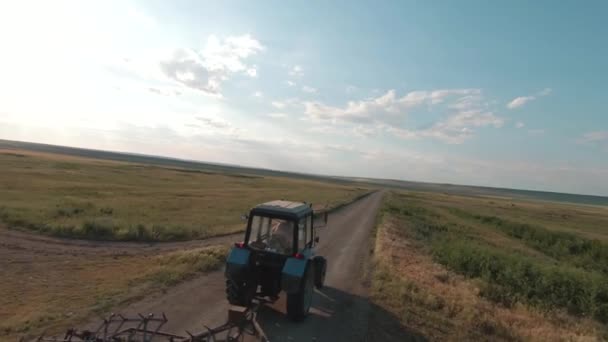 農場沿いの狭い道を田舎を走るトラクター。撃たれた。青空に向かって移動する古いトラクターマシンの空中ビュー. — ストック動画