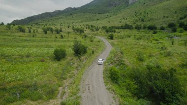 Yeşil dağların yakınındaki yolda giden arabanın üst görüntüsü. Başla. Dağ bölgelerinde güzel bir araba yolculuğu. Tek araba yeşil dağların arka planında ilerliyor.