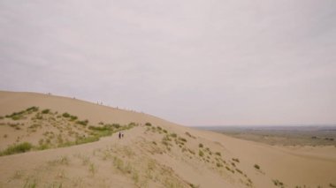 İnsanlar kumlu tepe boyunca yürür. Başla. Turistler çölde kum tepelerinde yürürler. Bulutlu havada sonsuz ufukta çölde yürüyorum.