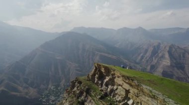 Yüksek dağların arkasındaki kayalık yamaçtaki gezginlerin en üst görüntüsü. Başla. Hava perdesiyle tepeden dağa nefes kesici bir manzara. Güneşli bir günde hafif sisli yüksek yeşil dağlar