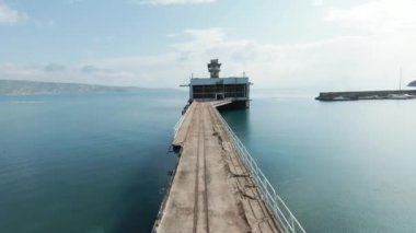 Harap olmuş eski bir iskele ve gök mavisi sonsuz bir deniz manzarası. Vuruldu. Mavi arka planda terk edilmiş dar bir iskele boyunca uçuyorum..