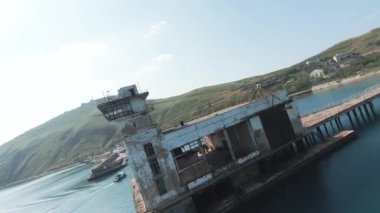 Uzun bir iskeleye inşa edilmiş terk edilmiş eski bir binanın havadan görüntüsü. Vuruldu. Arka planda mavi deniz ve yeşil dağlar olan deniz manzarası.