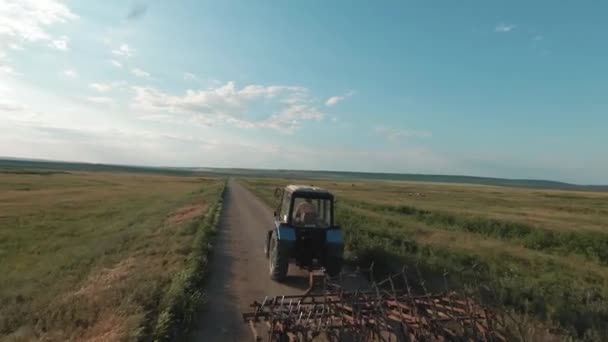 一辆拖拉机沿着农田在乡间一条狭窄的路上开着。射击。一架旧拖拉机驶向蓝天的空中景象. — 图库视频影像