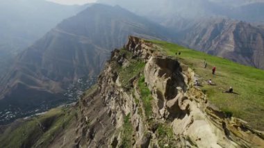 Yüksek dağların arkasındaki kayalık yamaçtaki gezginlerin en üst görüntüsü. Başla. Hava perdesiyle tepeden dağa nefes kesici bir manzara. Güneşli bir günde hafif sisli yüksek yeşil dağlar