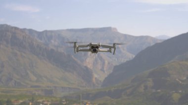 Dağın arka planında dört kopter uçuyor. Başla. Dağın arka planında uçan kuadrokopter görüntüsü. Quadcopter, güneşli bir günde dağ manzaralarının fotoğraflarını çeker.