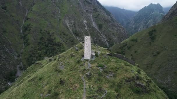 Luchtfoto van de oude begrafenis constructie Tsoy Pede, De Tsjetsjeense Republiek, Rusland. Actie. Witte toren op de top van een groene heuvel omringd door bergen. — Stockvideo