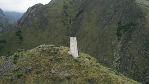 Luchtfoto van de oude begrafenis constructie Tsoy Pede, De Tsjetsjeense Republiek, Rusland. Actie. Witte toren op de top van een groene heuvel omringd door bergen. — Stockvideo