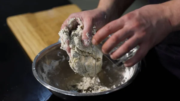 Homme pétrissant la pâte avec ses mains dans un bol en métal à la cuisine. L'art. Un cuisinier préparant la pâte, mélangeant les ingrédients avec ses mains. — Photo