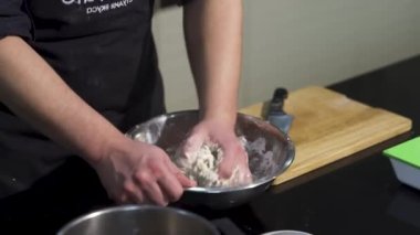 Mutfakta elleri metal bir kasede hamur yoğuran bir adam. - Sanat. Hamur hazırlayan bir aşçı. Malzemeleri elleriyle karıştırıyor..