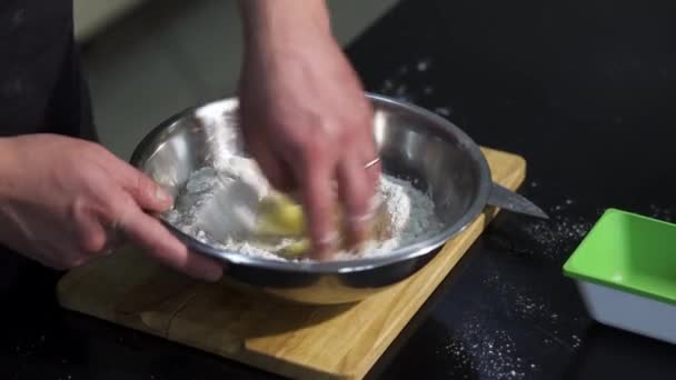 Primer plano de las manos masculinas amasando la masa con harina y huevos. Art. Mezclar los ingredientes en un recipiente de metal colocado en una tabla de madera con las manos. — Vídeos de Stock