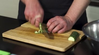 Ahşap bir tahtada soyulmuş salatalık kesen bir adam. - Sanat. Erkek şefin yemek hazırlarken ve sebze kesmek için çelik bıçak kullanırken yakın plan..