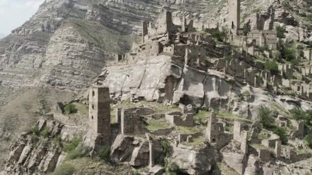 Vista aérea de un antiguo pueblo de piedra abandonado con edificios en ruinas. Acción. Acantilado rocoso con viejas torres y construcciones en un día soleado, concepto de arqueología. — Vídeo de stock