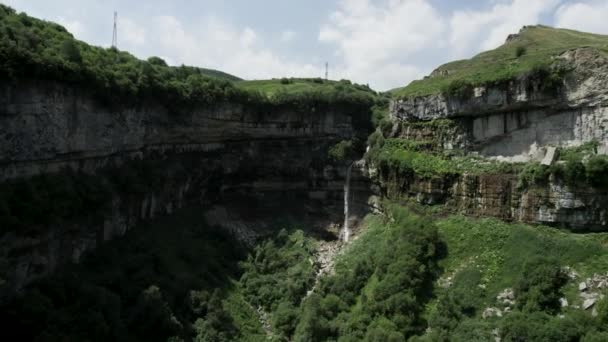 Aerial view over stunning natural landscape with summer huge rock formations and a waterfall. Action. Flying above green slopes covered by grass and trees. — Stock Video