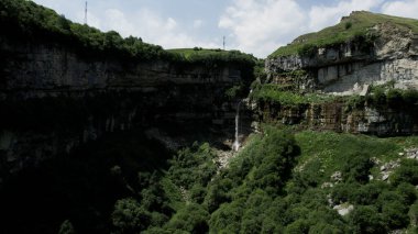Yazın muazzam kaya oluşumları ve bir şelaleyle baş döndürücü doğa manzarası. Başla. Çimlerle ve ağaçlarla kaplı yeşil yamaçların üzerinde uçuyorlar..
