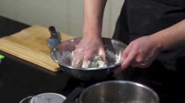 Mutfakta elleri metal bir kasede hamur yoğuran bir adam. - Sanat. Hamur hazırlayan bir aşçı. Malzemeleri elleriyle karıştırıyor..