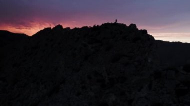 Güneşin doğuşunun önündeki dağın tepesindeki insanların havadan görünüşü. Başla. Siyah kaya siluetiyle çelişen renkli gökyüzü.