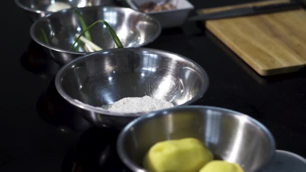 Vista de mesa com diferentes ingredientes em tigelas. Arte. Close up de placas de metal profundo com farinha, batata, cebola verde perto de uma tábua de corte de madeira, conceito de cozinhar alimentos. — Vídeo de Stock