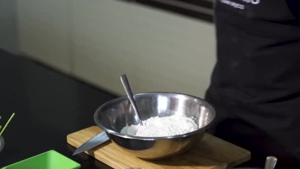 Sluit de mannelijke handen en voeg zout toe aan de bloem voor het kneden van het deeg. Kunst. Mengen van ingrediënten in een metalen kom geplaatst op een houten plank met een lepel. — Stockvideo