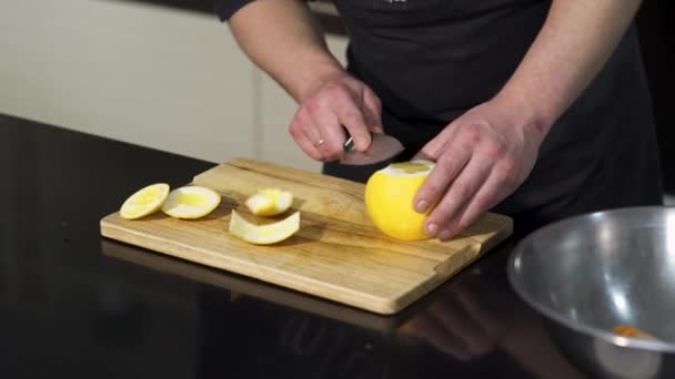 Großaufnahme eines männlichen Kochs, der mit einem Stahlmesser auf einem Holzbrett eine frische Orangenfrucht schält. Kunst. Konzept veganer Ernährung, Vitamine und Kochen. — Stockvideo