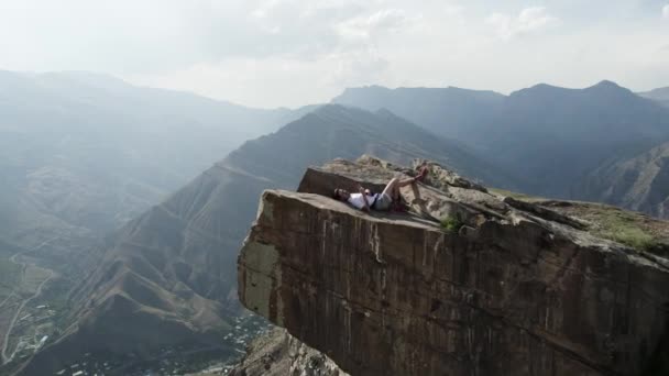 Widok z lotu ptaka młodego człowieka leżącego na szczycie epickiej skały. Akcja. Pojęcie wolności i przygody, podróżowanie w górach. — Wideo stockowe