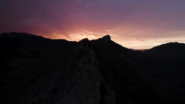 Vista aérea de las personas en una cima de la montaña frente a la impresionante salida del sol. Acción. Cielo colorido que contrasta con la silueta de roca negra. — Vídeos de Stock