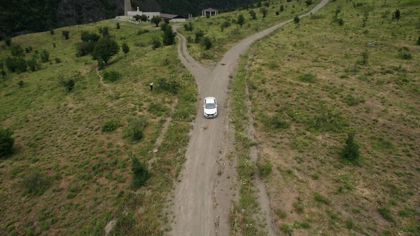 Vue aérienne d'une voiture de tourisme blanche conduisant sur une route rurale étroite dans les montagnes. L'action. Un véhicule se déplaçant le long d'arbres rares et de pentes verdoyantes. — Photo