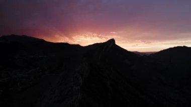 Güneşin doğuşunun önündeki dağ sırasının havadan görünüşü. Başla. Siyah kaya siluetiyle çelişen renkli gökyüzü.