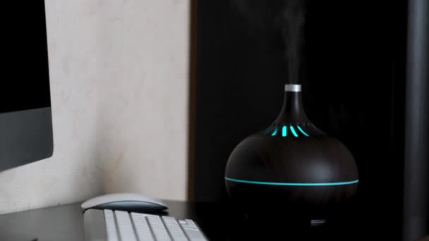 Humidificador esparciendo vapor en casa, detalles del interior de un apartamento moderno. Concepto. Humidificador ultrasónico de pie en una mesa cerca de la computadora y el teclado. — Vídeo de stock