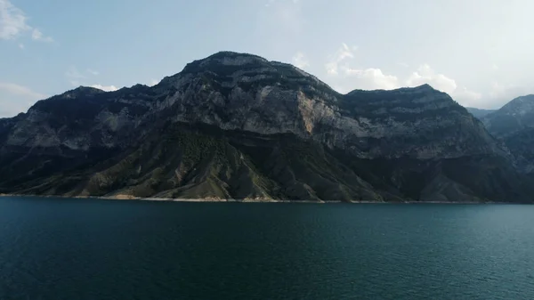 Natuurlandschap met een turquoise waterreservoir en een enorme berg. Actie. Rustige blauwe rivier en een hoge heuvel op blauwe lucht achtergrond. — Stockfoto