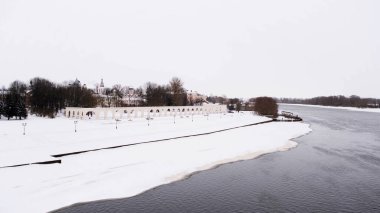 Kış nehrinin üzerinde uçmak kısmen buz ve karla kaplı bulutlu arka planda. Kavram. Kel ağaçlı küçük bir kasabada soğuk hava.