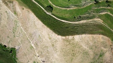 İlkbaharda Slovenya 'daki ulusal parktaki bir dağın havadan görünüşü. Başla. Yeşil çimlerle kaplı bir yamaçla yüksek bir tepenin üzerinde uçuyor ve dar yollar ve taşlarla ve kumla kaplı başka bir yokuş..