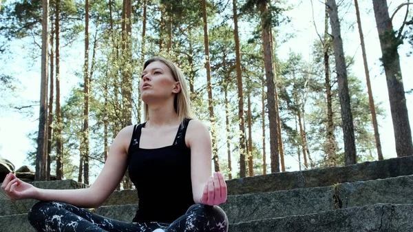 Mujer feliz profundamente conectada con la naturaleza siente unidad y meditación en el bosque al aire libre. Concepto. Chica rubia en traje deportivo sentado en escaleras de hormigón en meditación en un día de verano. — Foto de Stock