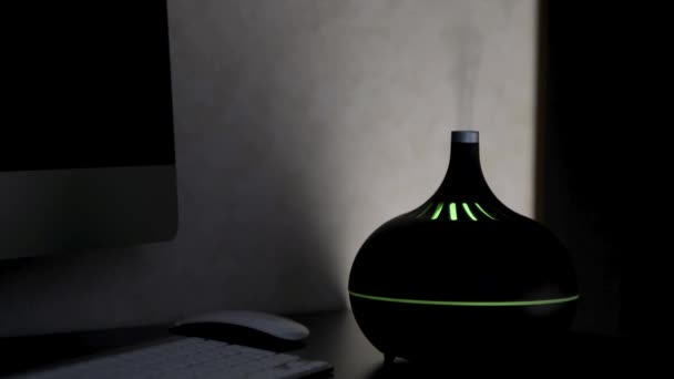 Diffuseur d'huile d'aromathérapie avec lumière LED colorée à partir de laquelle la vapeur sort sur un fond sombre. Concept. Humidificateur aromatique sur une table à la maison. — Video